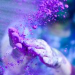 Close-up of hands throwing vibrant purple powder outdoors, capturing motion and color.